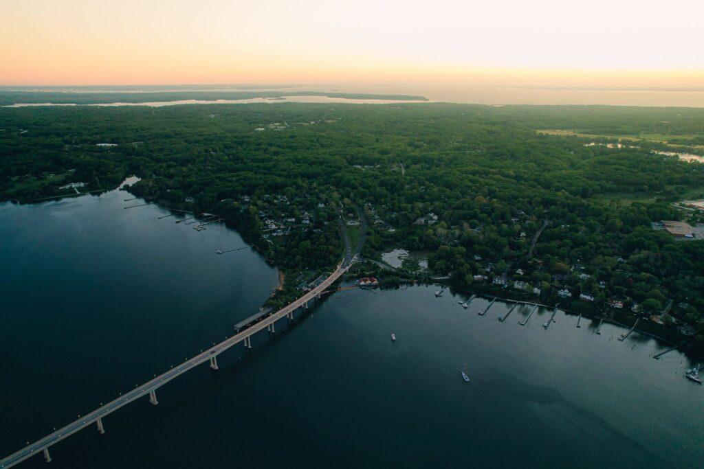 Aerial view of a wide river winding past wooded shoreline and a long bridge at dusk