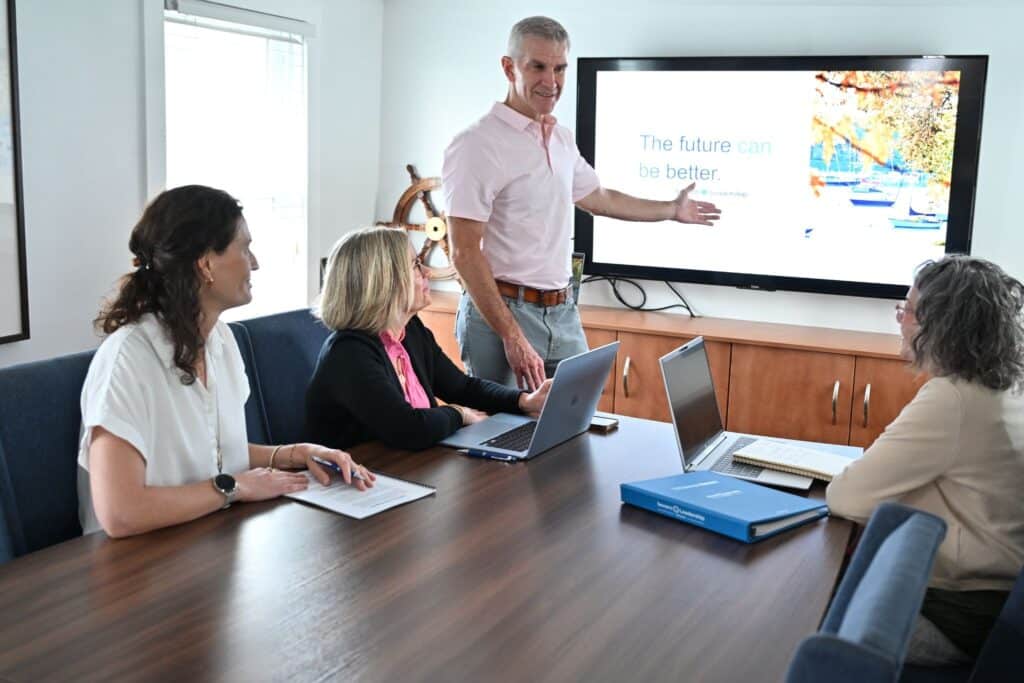Facilitator presents to a small team seated around a conference table with program binders