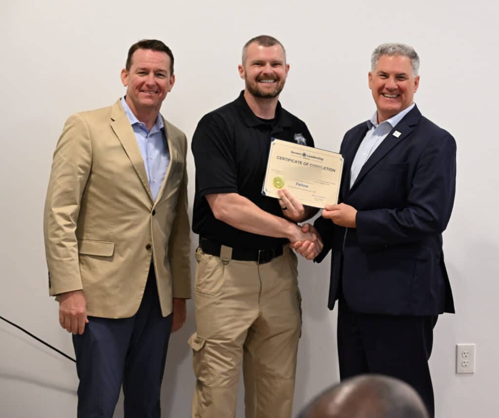 Fellow receives his certificate with a handshake from mentors at a Severn Leadership Group graduation in Annapolis