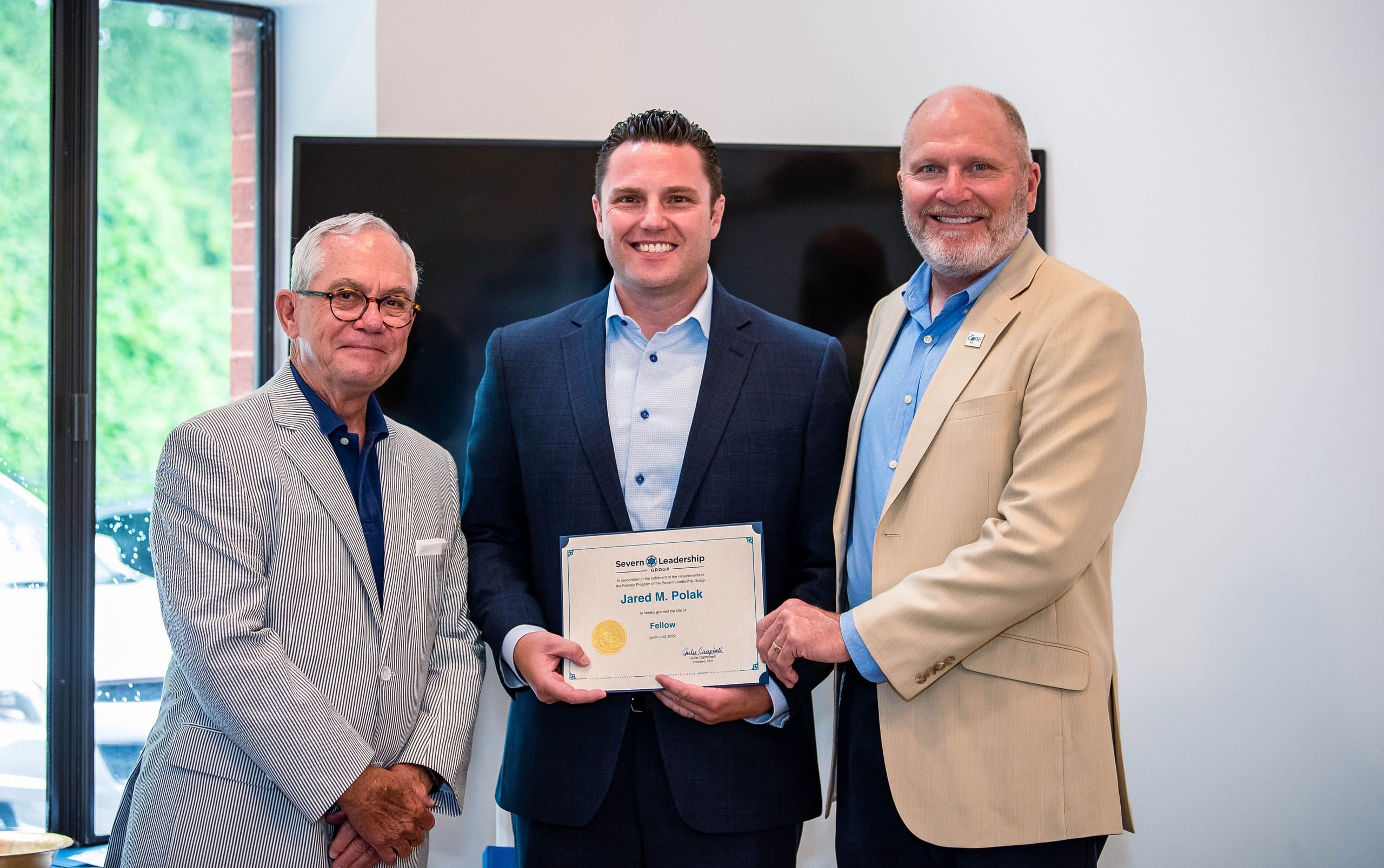 Fellow holds his certificate between two mentors at a Severn Leadership Group graduation in Annapolis
