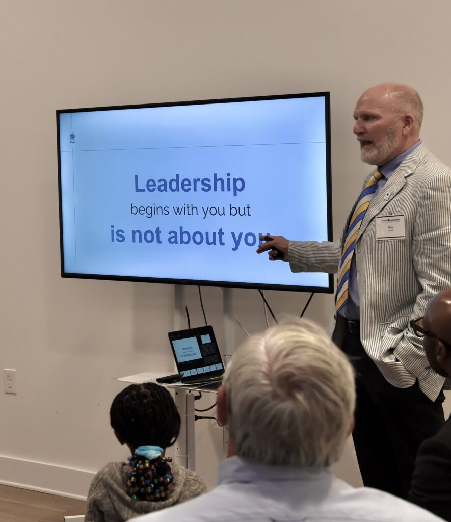 Speaker points to a slide reading Leadership begins with you but is not about you
