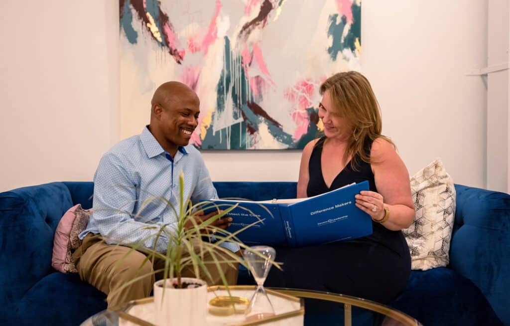 Mentor and Fellow look over a blue program binder together on a couch during a mentoring conversation