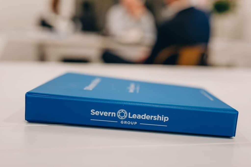 Blue Severn Leadership Group binder resting on a table with participants blurred in the background